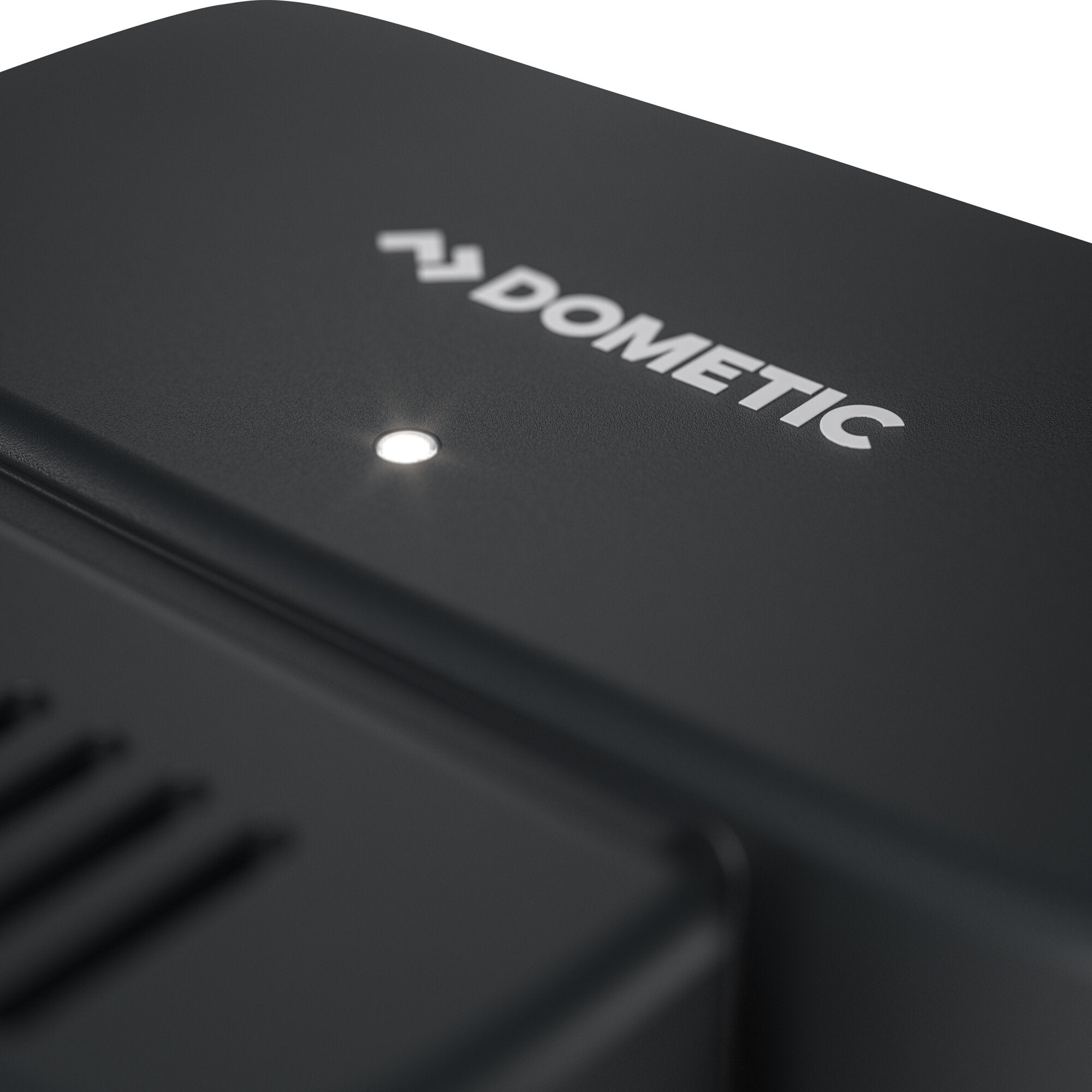 Nahaufnahme eines dunklen Gehäuses mit geprägtem DOMETIC-Logo und zwei kleinen LEDs, Fokus auf der Oberseite eines Luftreinigungssets