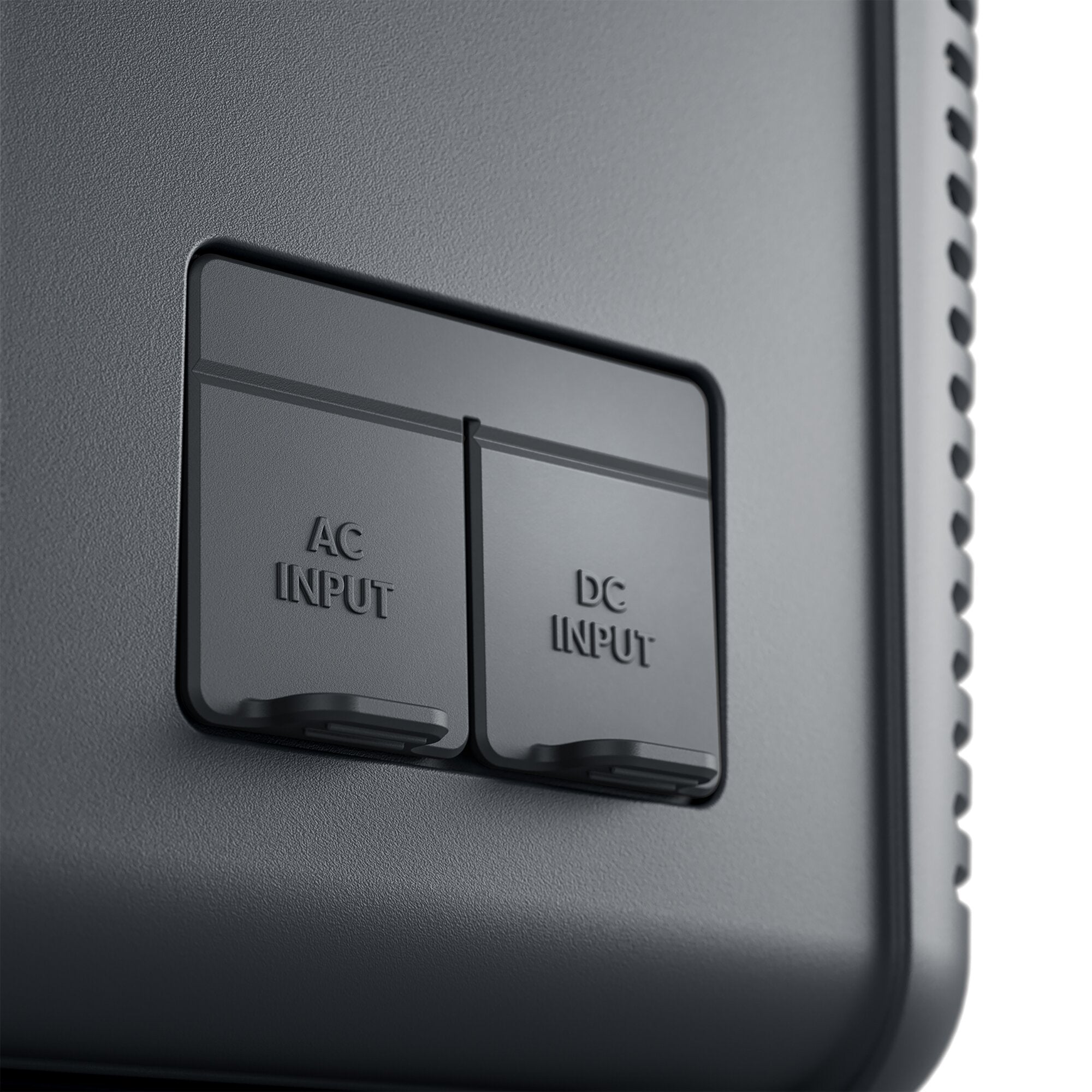 Detailaufnahme einer schwarzen Kompressor-Kühlbox: Vorderseite mit AC INPUT- und DC INPUT-Beschriftung, gerippter Rand und Griffmulde unten
