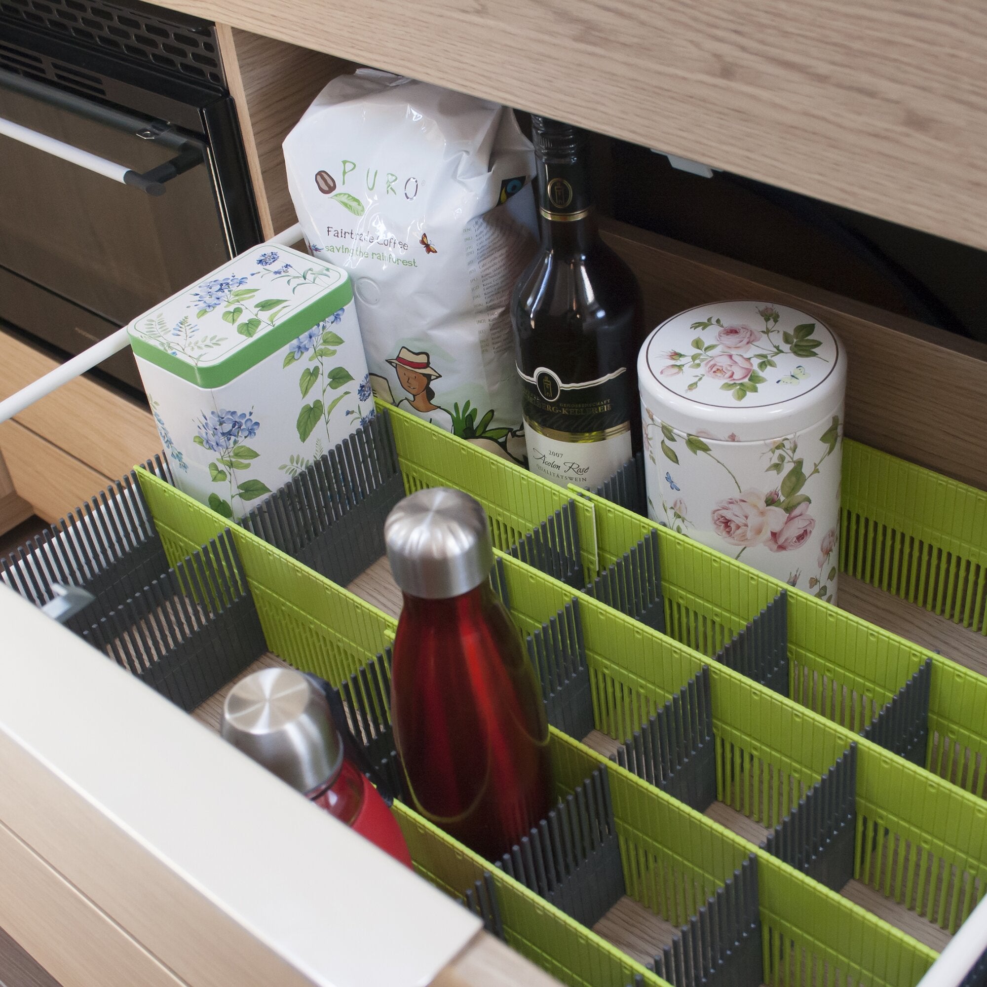 Unterbau eines Küchenschranks mit limegrüner Stauleiste MAXXI 100; grüne Trennwände bilden Flaschenfächer, daneben Weinflasche und Dosen mit Blumendekor