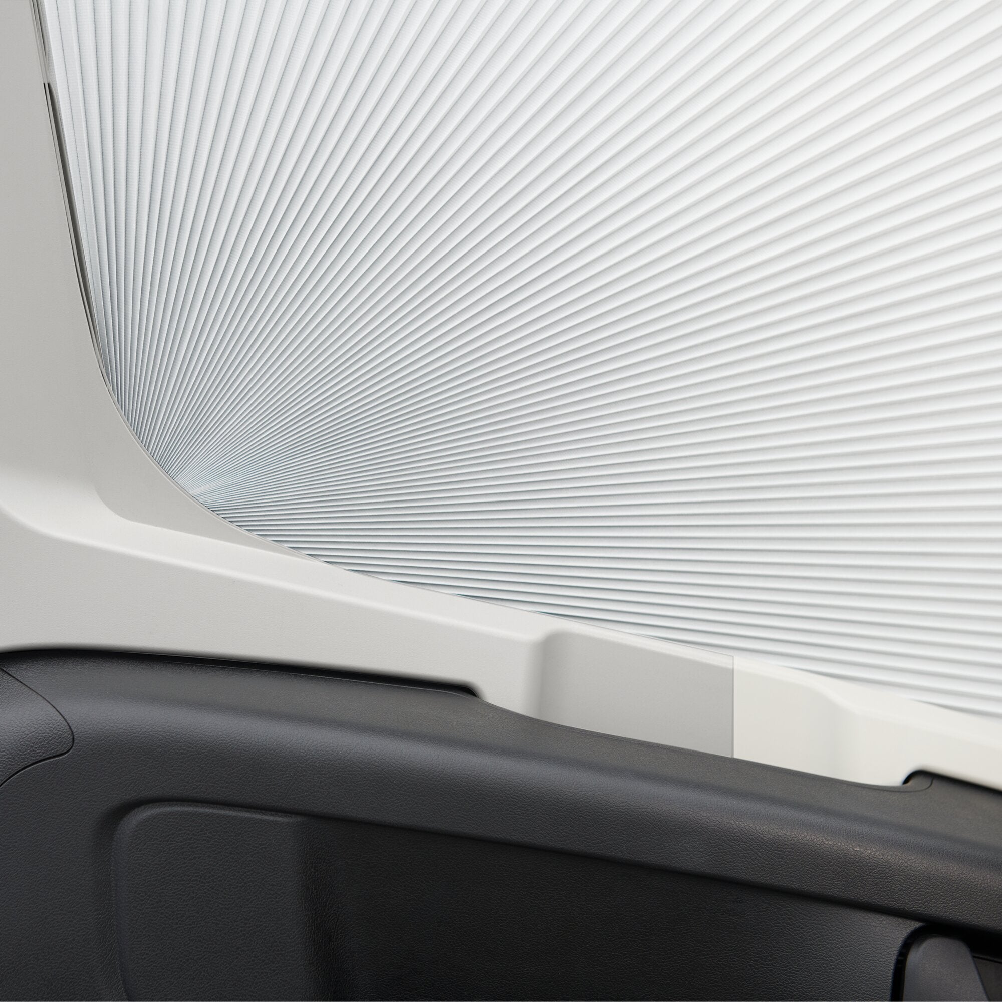 Innenraum eines Freizeitfahrzeugs mit weißem, gefaltetem Sonnenschutz am Seitenfenster, umlaufender Rahmen und dunkler Armaturenbereich darunter