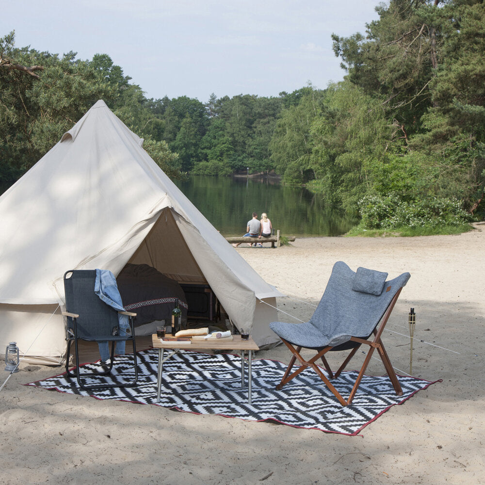 Relaxsessel Bloomsbury M aus grauem Stoff mit Holzrahmen neben einem cremefarbenen Zelt auf einem Teppich am Strand; zwei Personen am See