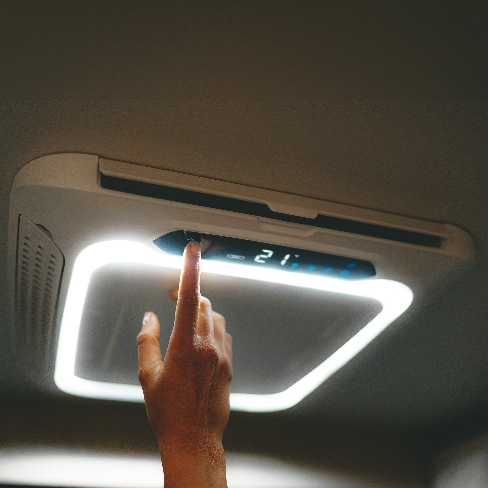 Fahrzeuginnenraum mit einer hellen runden Ringlicht-LED über dem Klimaanlagen-Bedienfeld; eine Hand zeigt mit dem Finger darauf