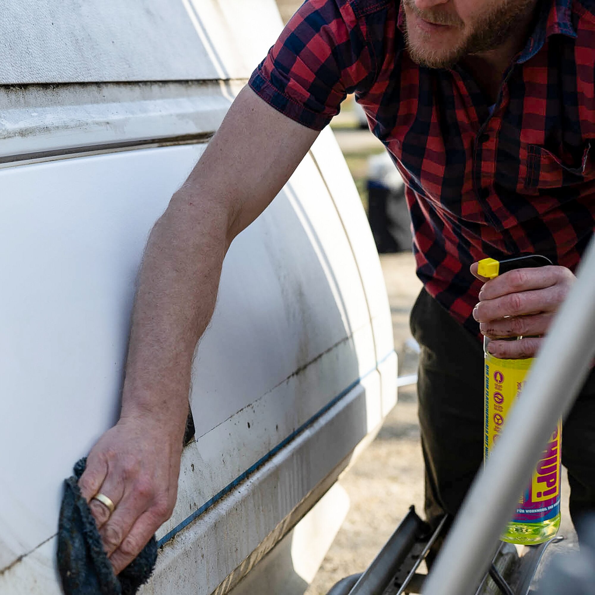 Mann in rotem Karohemd steht neben einem weißen Wohnmobil und hält eine gelb beschriftete 1-Liter-Flasche Caravan Spezialreiniger