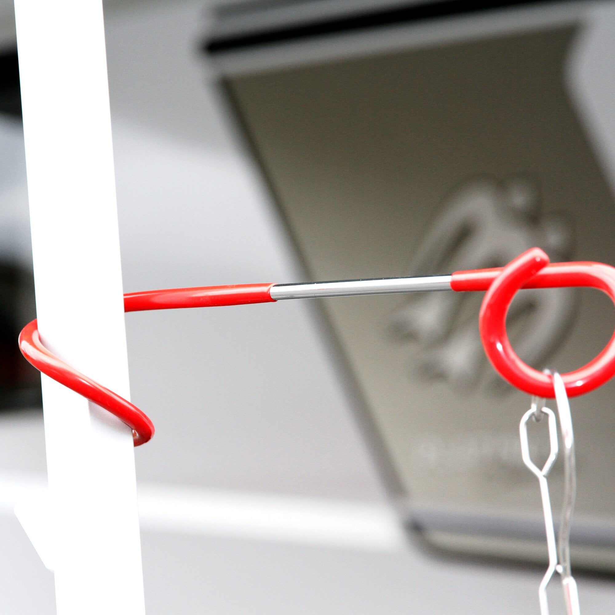 Detailaufnahme eines roten Unifix Universalhakens, gebogener Metalldraht mit Schlaufe an einer weißen Stangenkonstruktion, Hintergrund unscharf