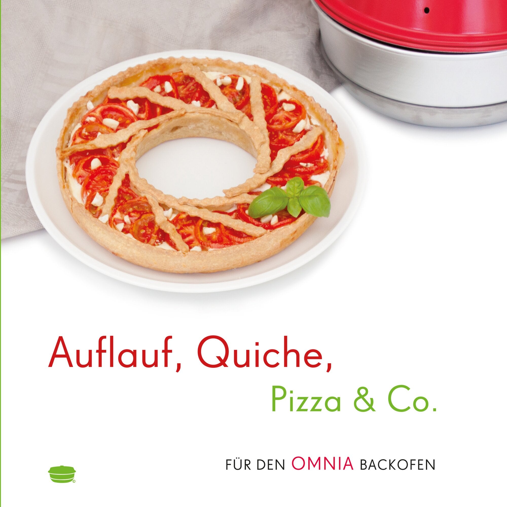 Runde Tomaten-Quiche mit Teiggitter, Tomatenscheiben, Käsewürfel und Basilikum auf einem weißen Teller – roter Ofen-Deckel im Hintergrund
