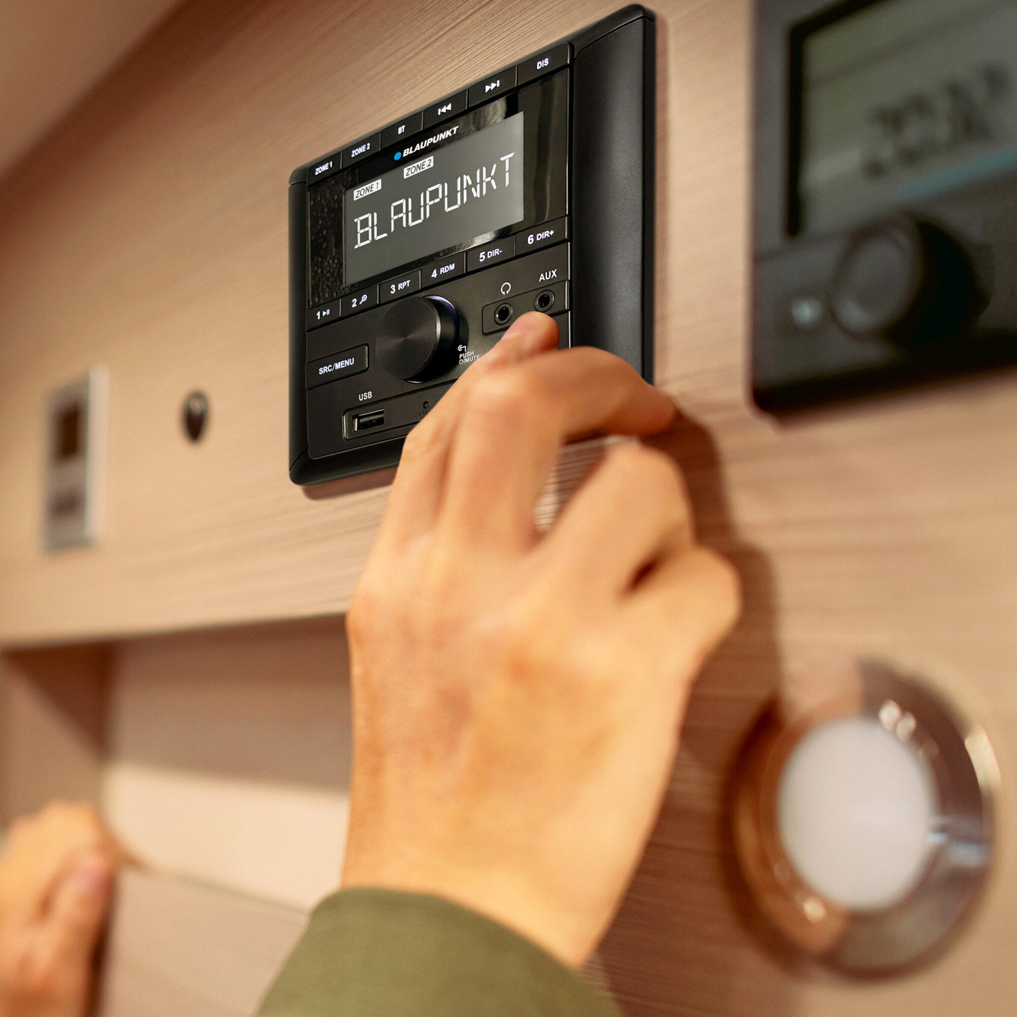 Seitennahe Nahaufnahme eines eingebauten Blaupunkt Camper BPA 3022 M Radios; Display zeigt Blaupunkt und Zonen, Hand am Knopf