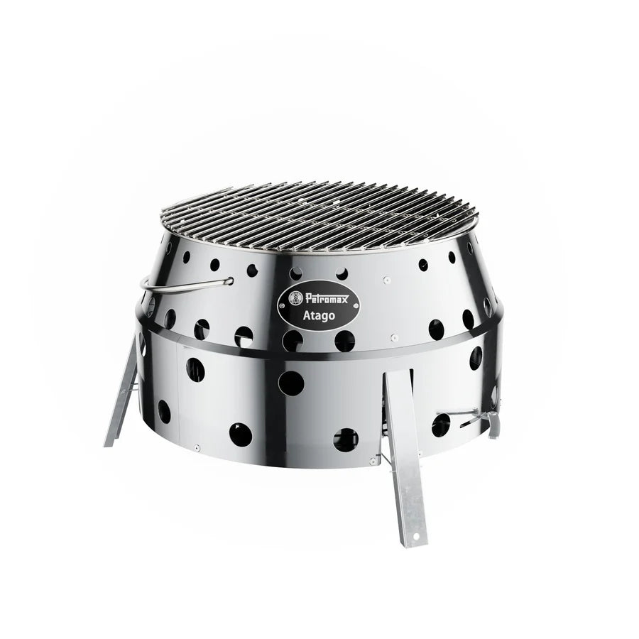 Runder silberner Petromax Atago Grill aus Edelstahl mit Luftlöchern und klappbaren Beinen, Gusseisengitter oben.