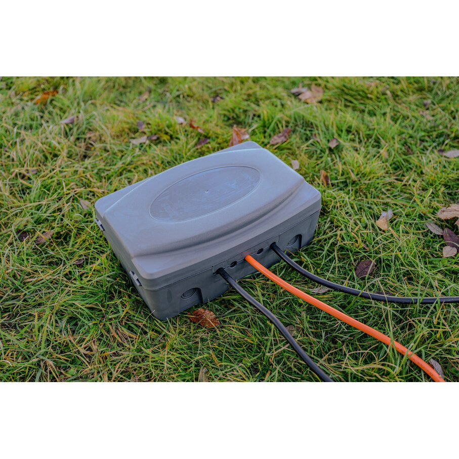 Graue Wetterschutz-Box IP54 mit ovalem Deckel liegt auf Gras, mehrere Kabel führen durch seitliche Öffnungen in die Box