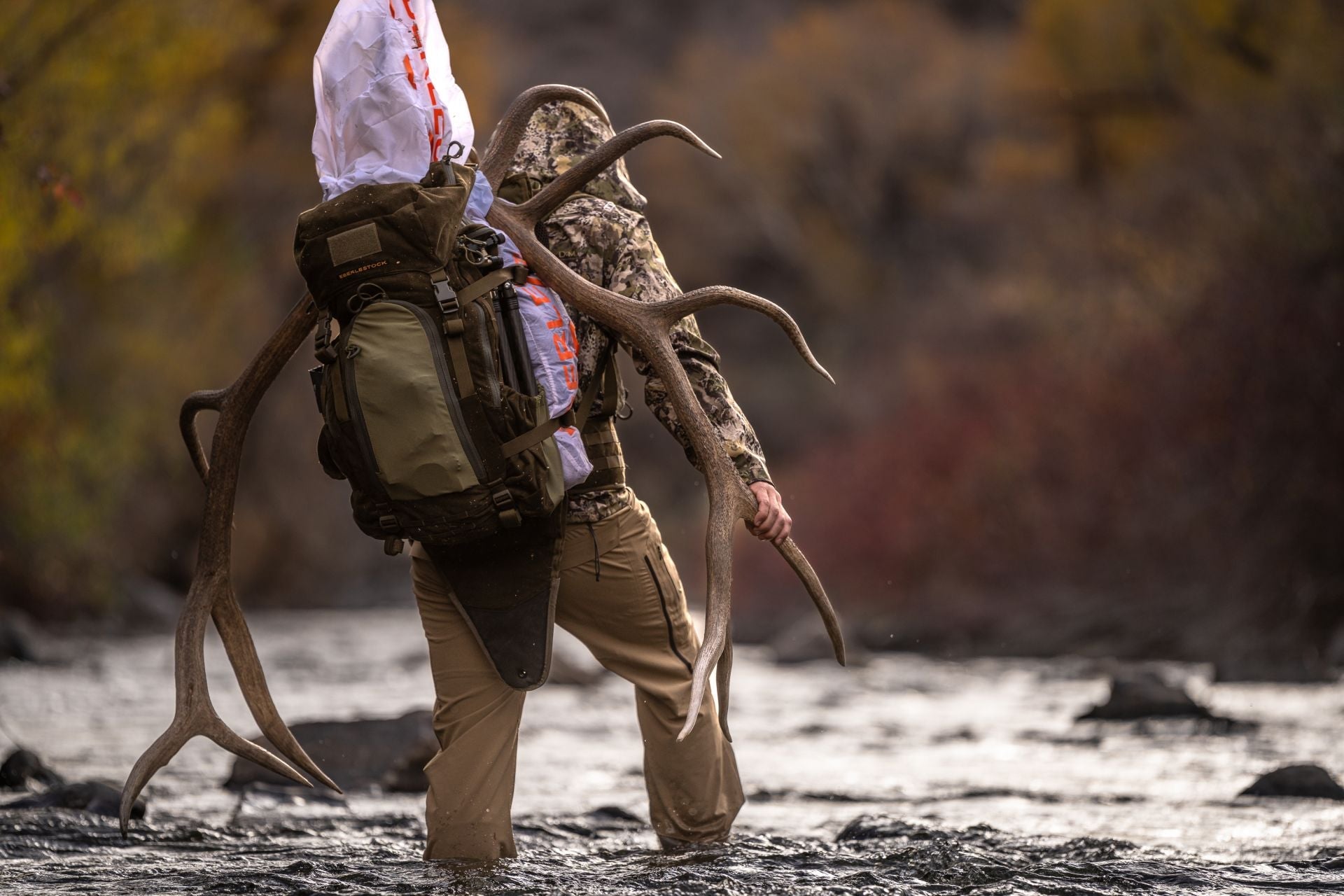 Jäger trägt dunkelolivenfarbenen Eberlestock M5 RMEF Team Elk V2 Jagdrucksack mit robustem Rahmen, hält großes Geweih am.