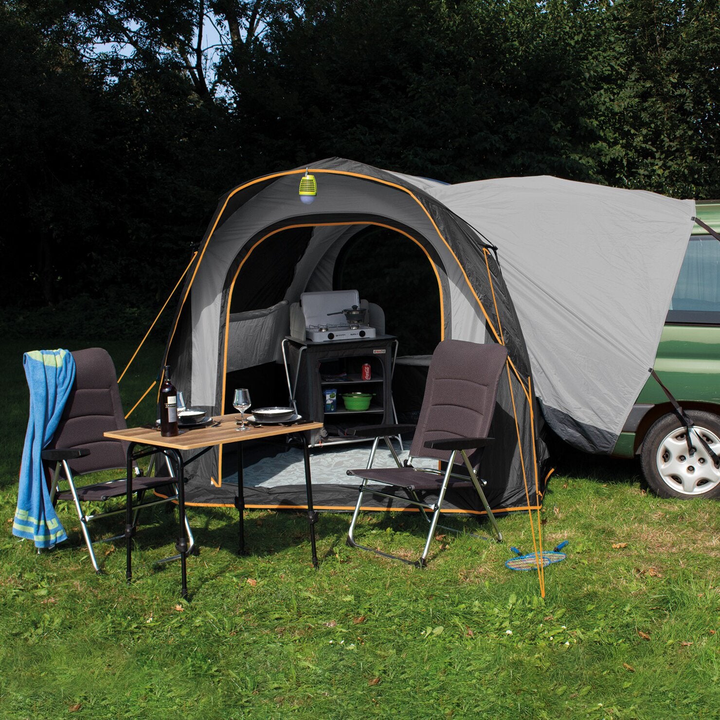 Heckzelt Cruiser SUV Air am Heck eines Campers, dunkelgraues Zelt mit orange Naht, Outdoor-Küche mit Grill, Tisch, Wein-Glas und Bierflasche