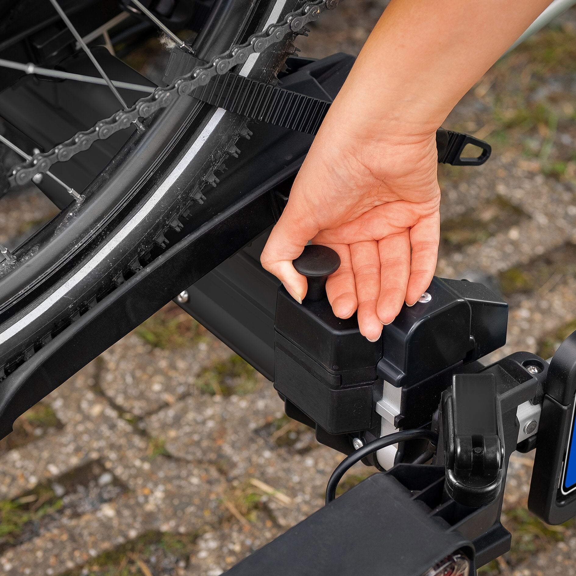 Schwarzer SD260 Fahrradträger an der Anhängerkupplung, Nahaufnahme der Montagebauteile; Hand greift einen runden Knopf, Kette und Rahmenteile sind sichtbar