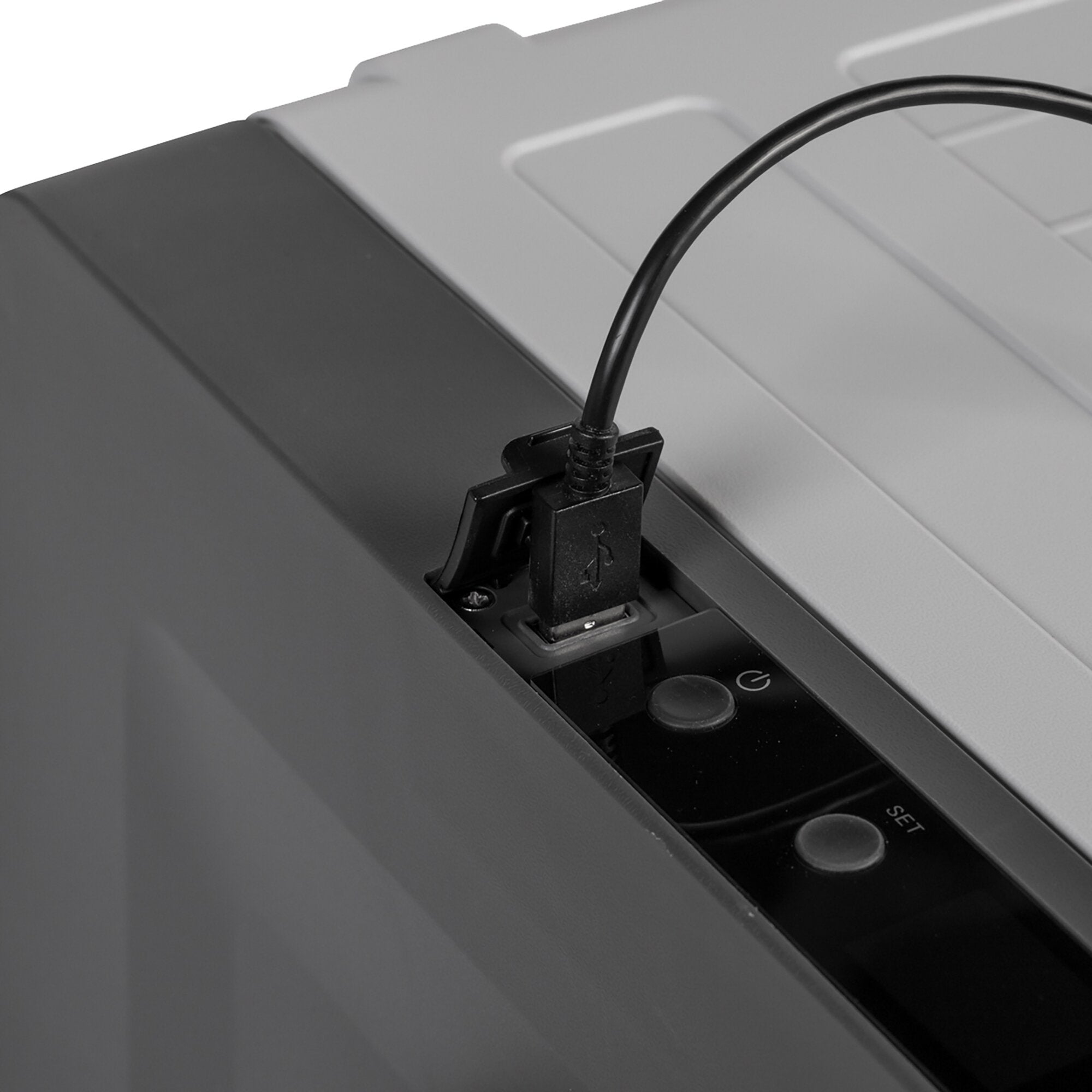 Nahaufnahme einer Kühlbox, an deren Bedienfeld ein schwarzes Netzkabel angeschlossen ist; graue Gehäuseoberfläche und sichtbare Tasten