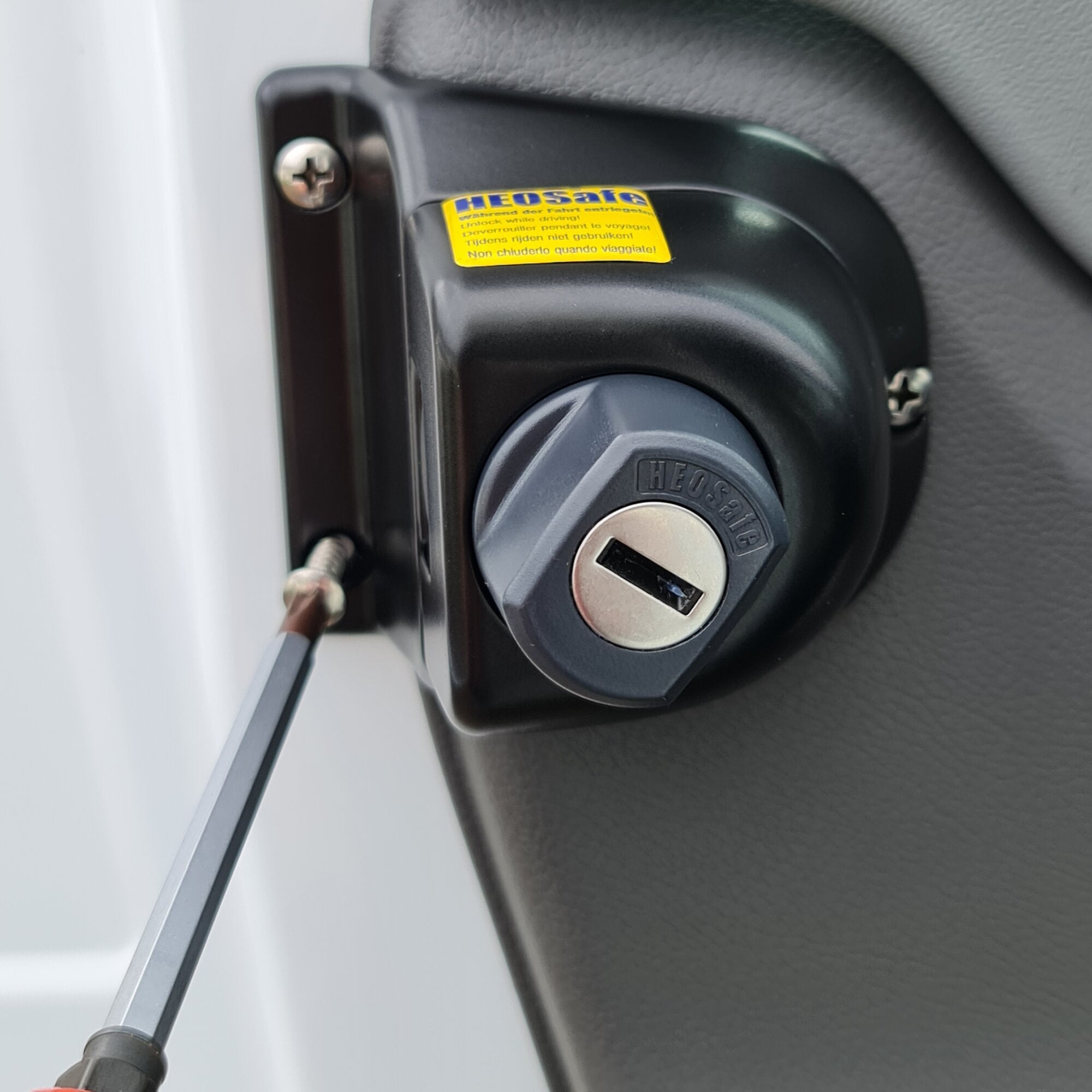 Detailansicht eines Diebstahlschutzschlosses an der Fahrertür des Ford Transit Gen7, schwarzes Gehäuse runder Zylinder gelber Warnaufkleber