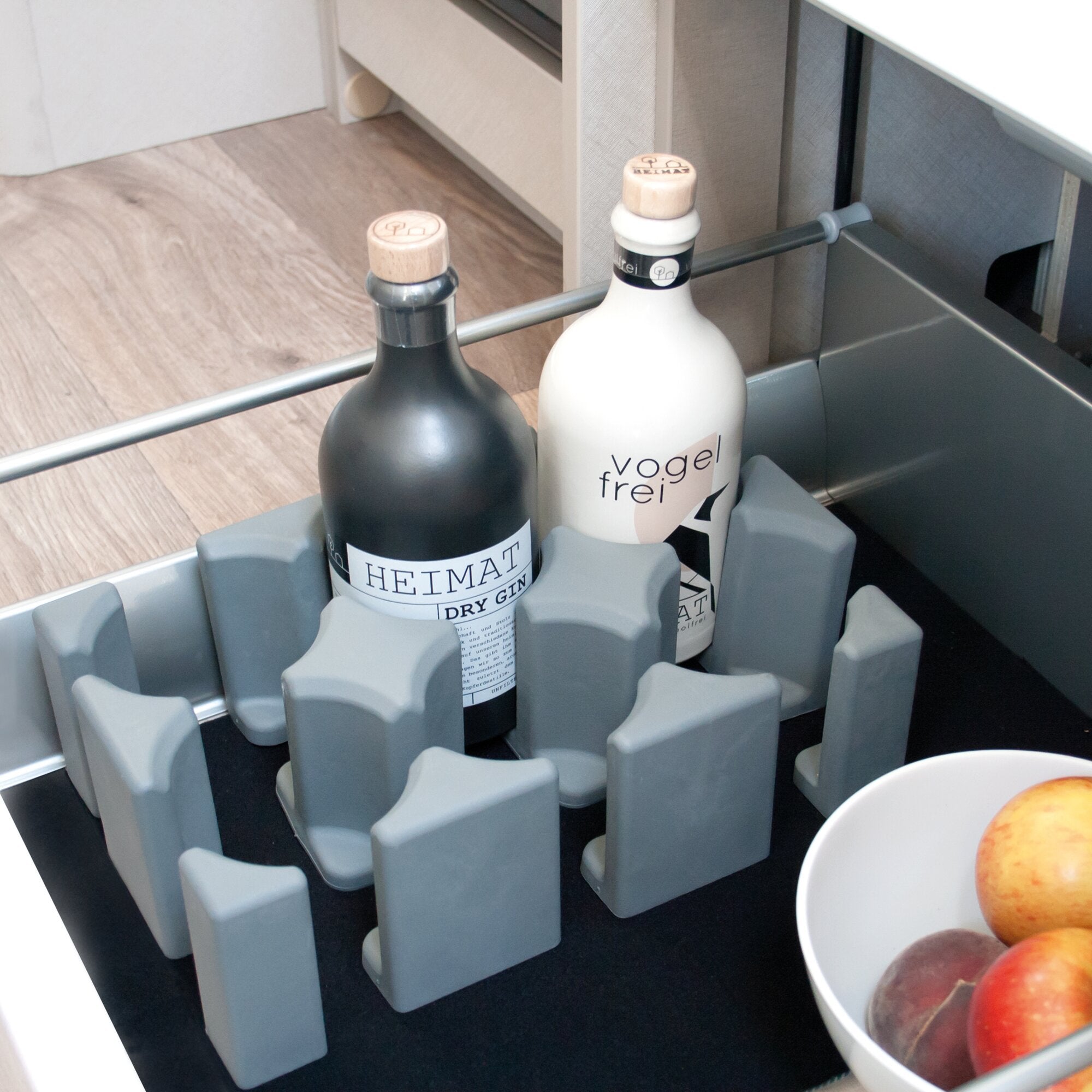 Zwei Ginflaschen stehen in einem grauen Flaschenhalter aus Kunststoff, links dunkle Flasche mit Holzstopfen, rechts helle Flasche mit Vogel-Frei-Label