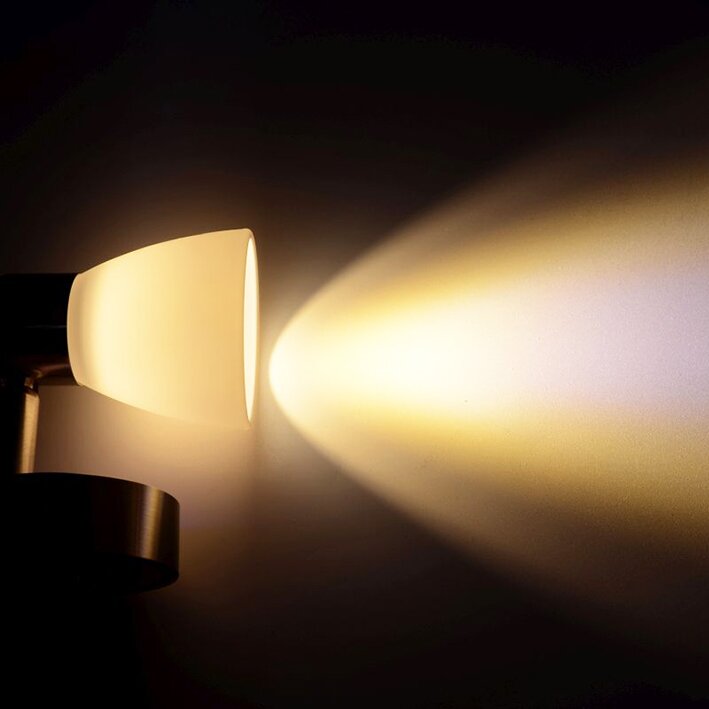 Aufbau-Leseleuchte mit weißem, konischem Lampenschirm und dunklem Sockel, warmes Licht breitet sich als großer Lichtkegel an die Wand aus