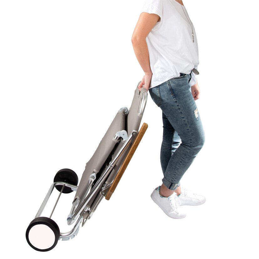 Zusammengefaltete Strandliege Beach Trolley mit Metallrahmen, Holzgriff und zwei Rädern wird von einer Person in Jeans und T‑Shirt gehalten
