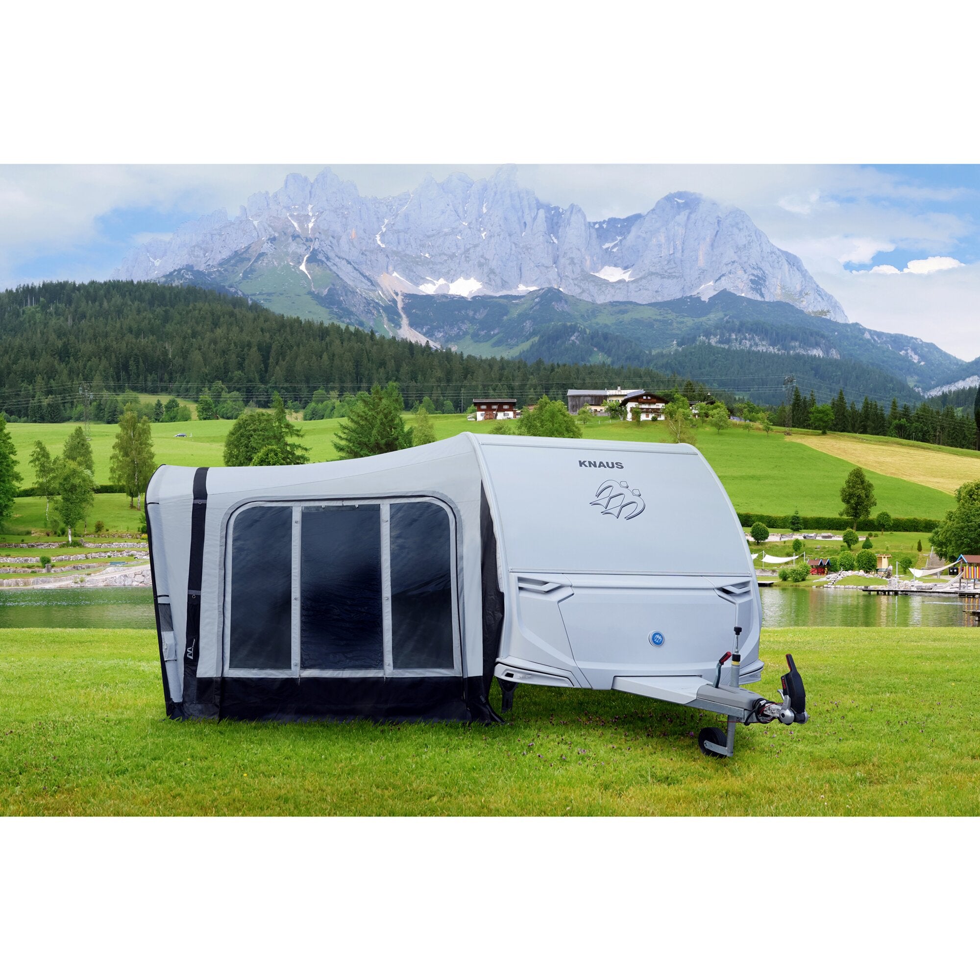 Reisevorzelt in hellgrau mit dunklen Fenstern, an einem KNAUS Wohnwagen befestigt, steht am See vor einer Berglandschaft