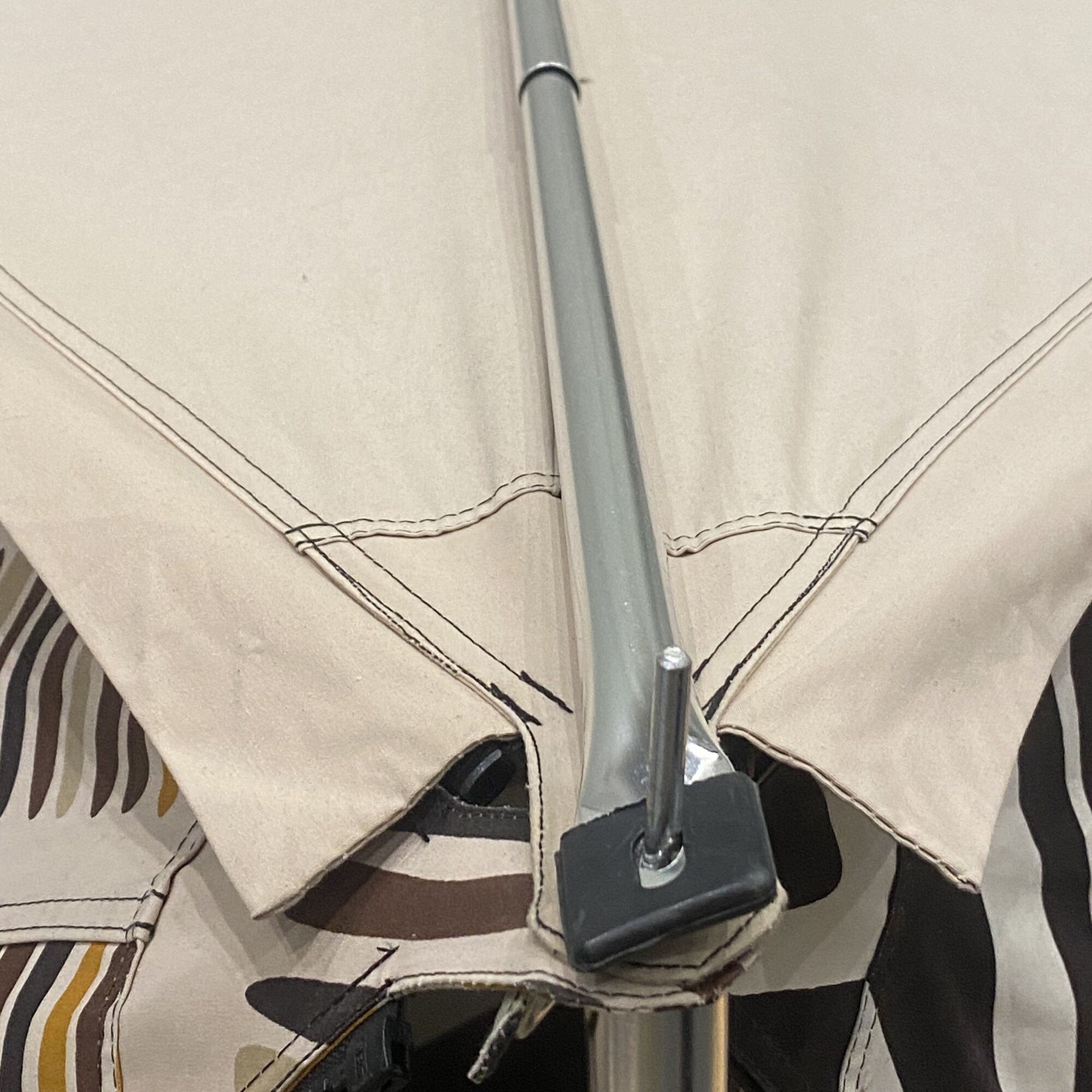 Detailaufnahme eines silbernen Alu-First-Spannstab mit schwarzer Kunststoffhalterung, vor braunem Karton mit sichtbaren Nahtlinien