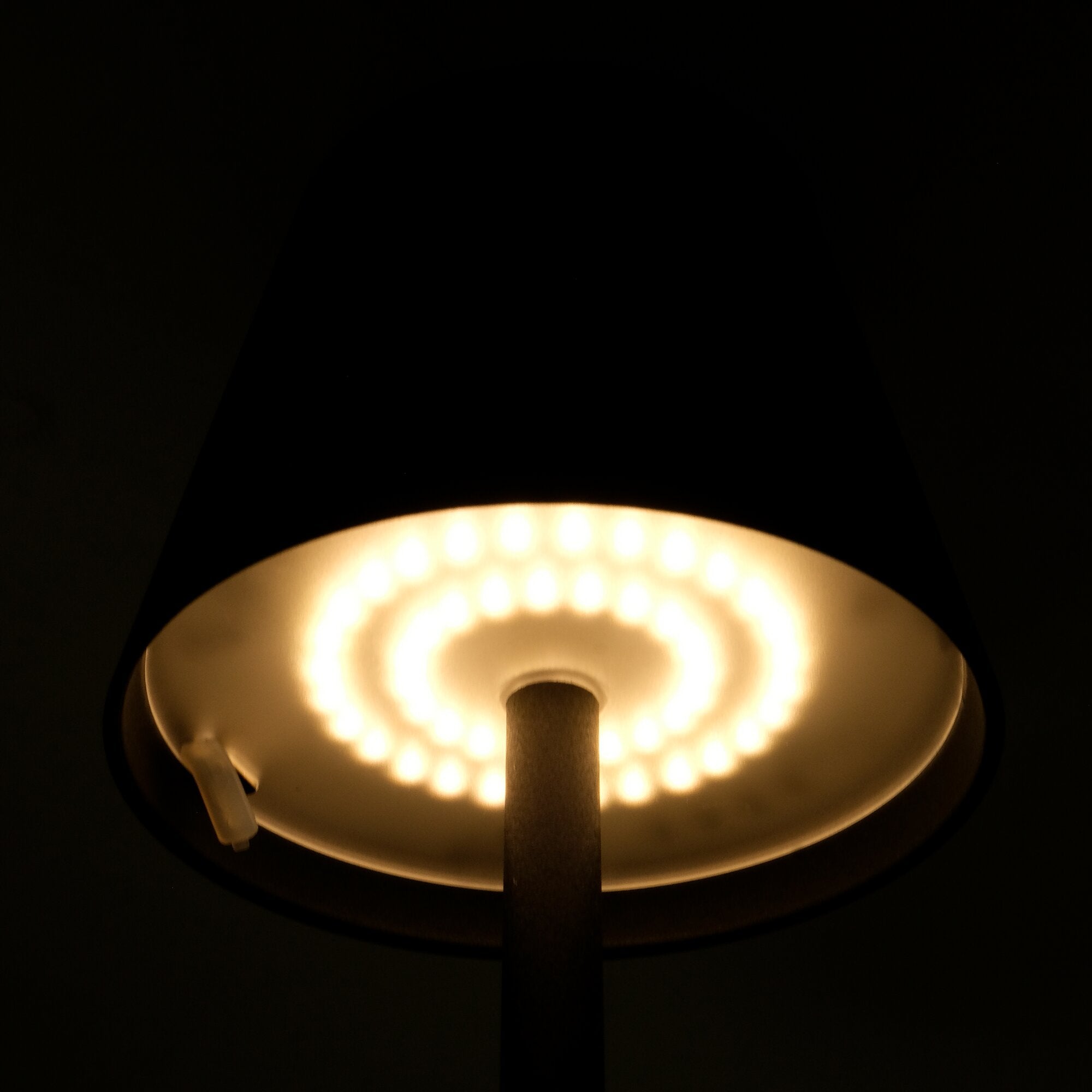 Detailaufnahme einer LED-Akku-Tischlampe Lucien in Schwarz; runder Lampenschirm mit LED-Ring und zentralem Stab, Kabel links sichtbar