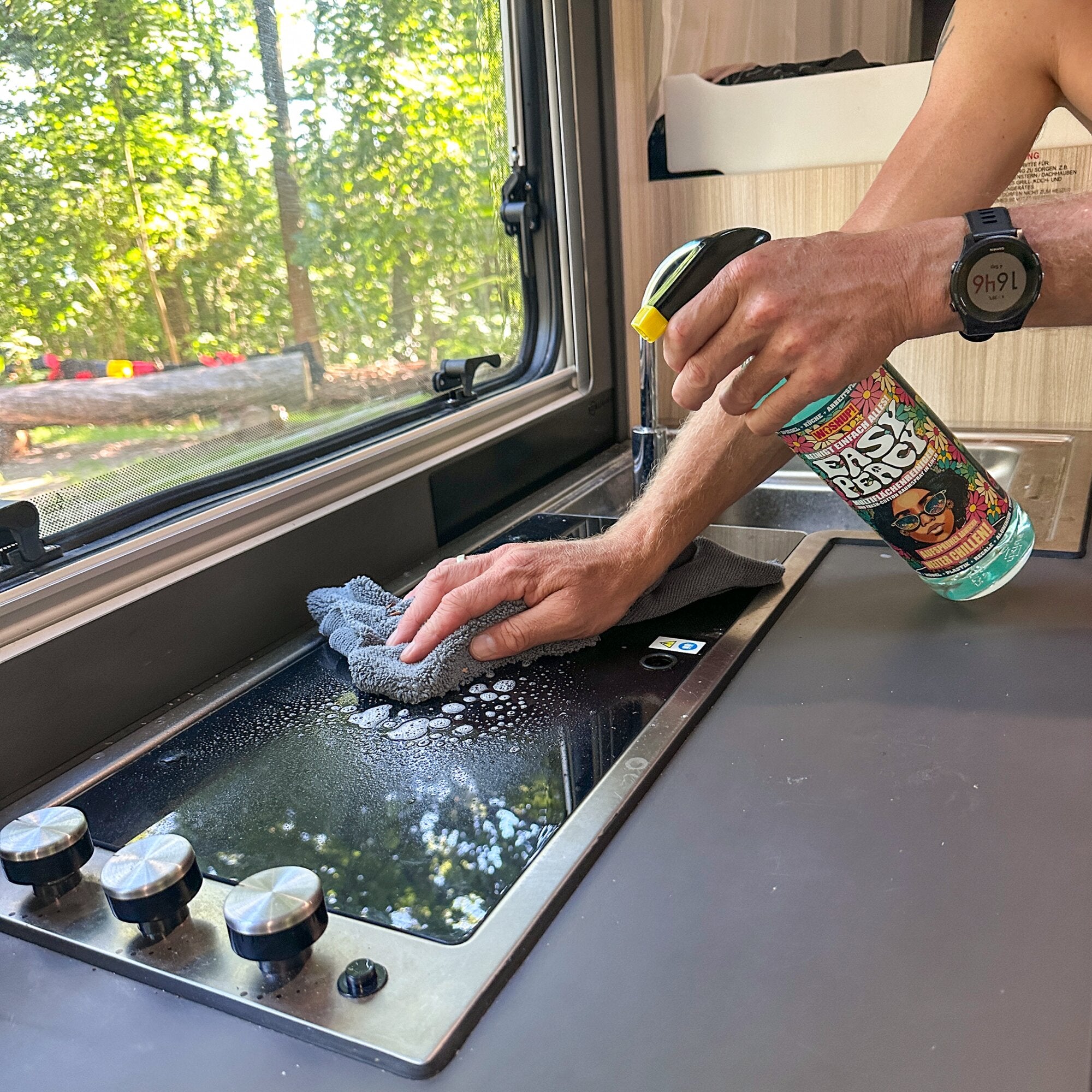 Person reinigt eine Camper-Küche mit einer gelben Sprühflasche Easy Peacy Multiflächen-Reiniger, 1 l, und wischt mit grauem Tuch