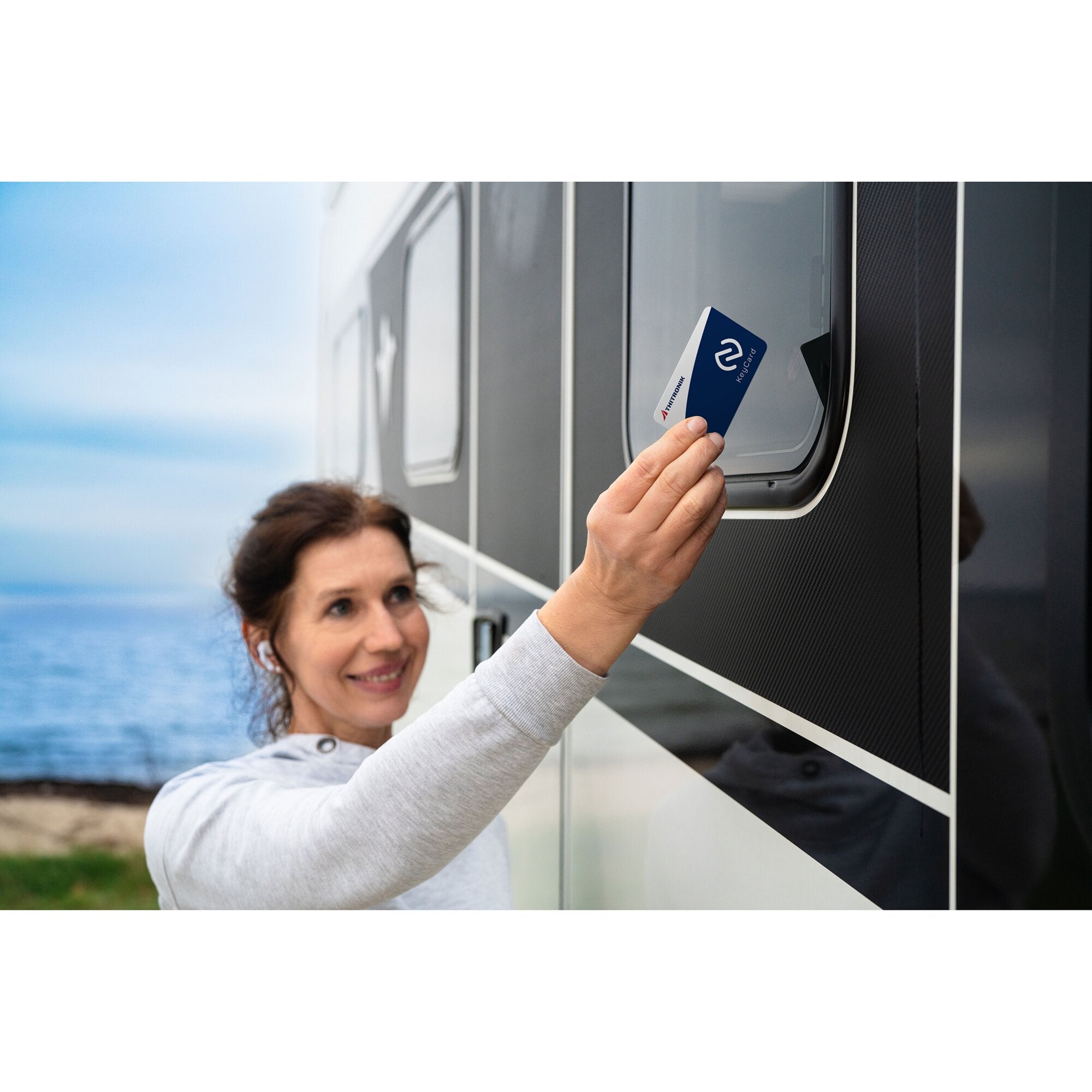 Eine Person hält eine blaue NFC-Transponderkarte vor ein Lesegerät an einer dunklen Gehäusefront, der kontaktlose Lesevorgang ist sichtbar