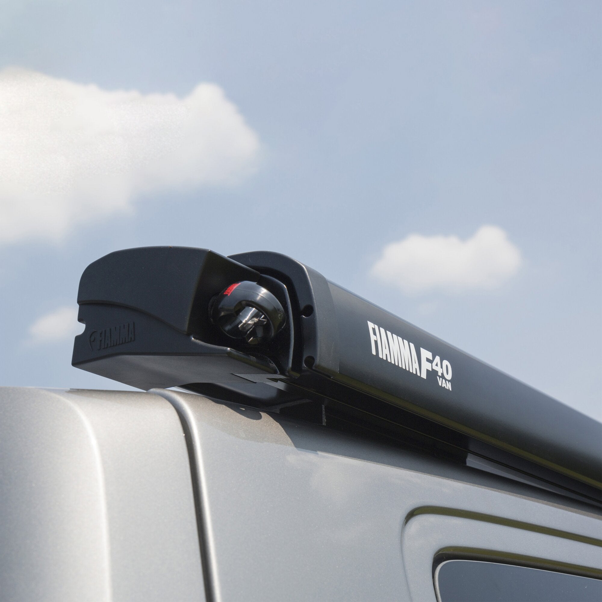 Detailaufnahme einer schwarzen Dachmarkise am Van, Gehäuse mit FIAMMA F40 VAN Schriftzug und rotem Einstellrad vor blauem Himmel