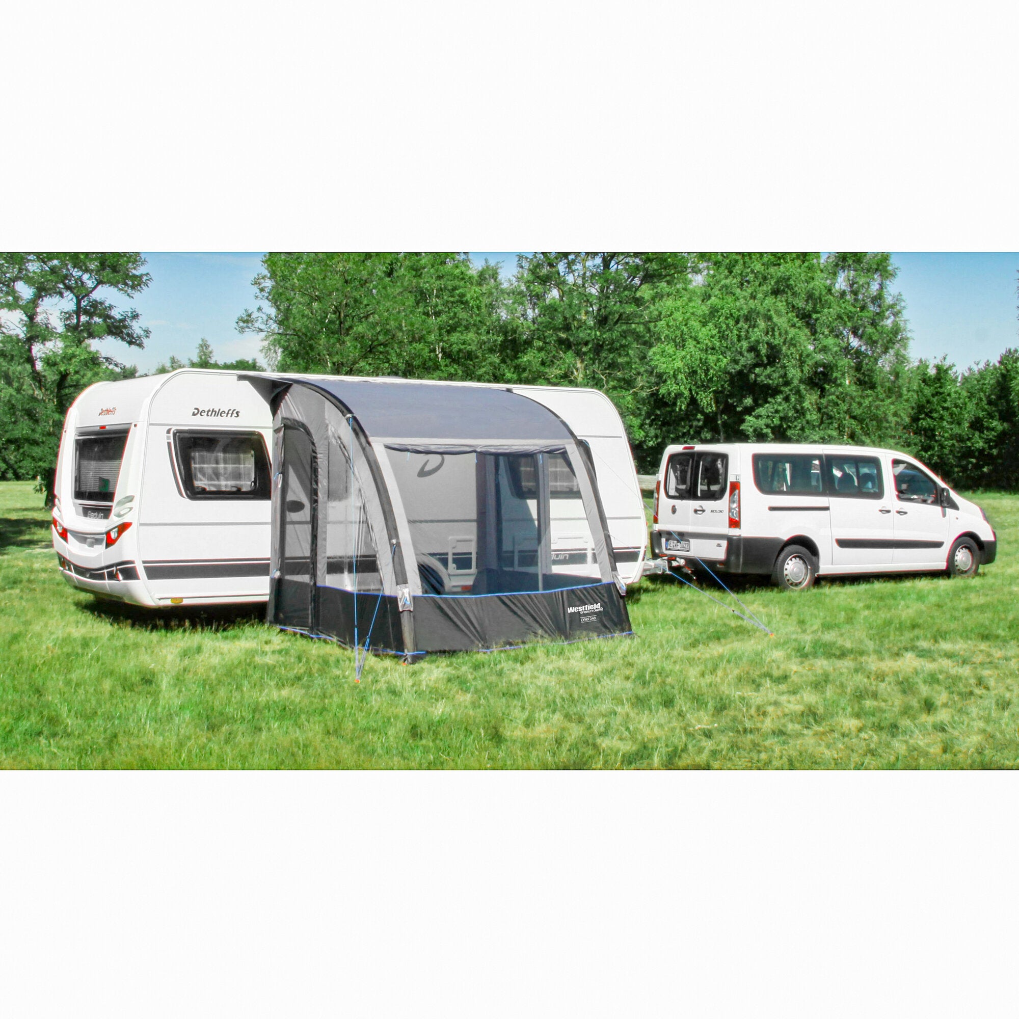 Weiße Wohnwagen am Campingplatz mit aufgebautem schwarzen Westfield Lynx 200 cm Teilzelt im Vordergrund, grüne Wiese und Bäume