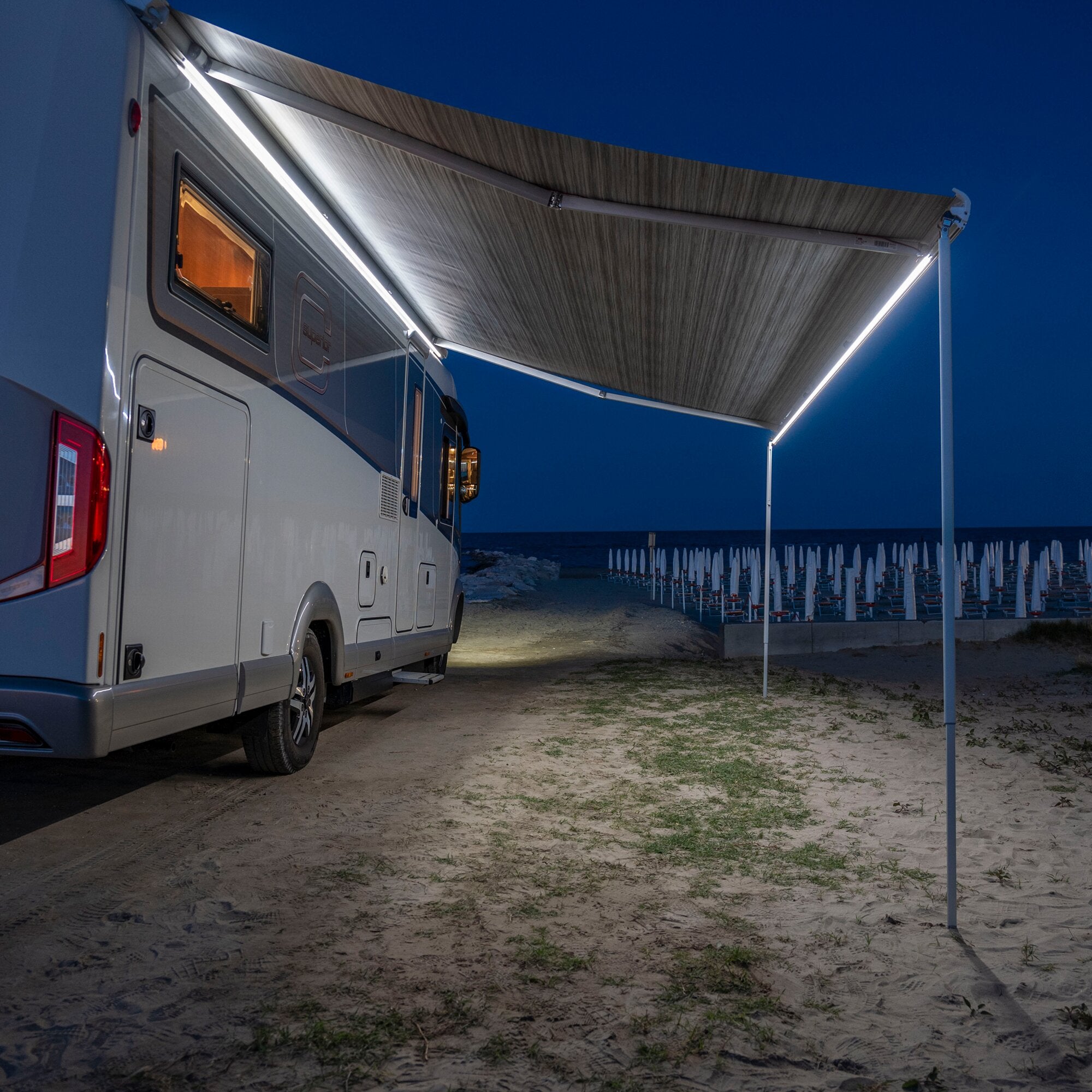 Abendliche Aufnahme eines Wohnmobils mit ausgefahrener Markise; eine helle LED-Lichtleiste verläuft längs der Kante und beleuchtet den Außenbereich