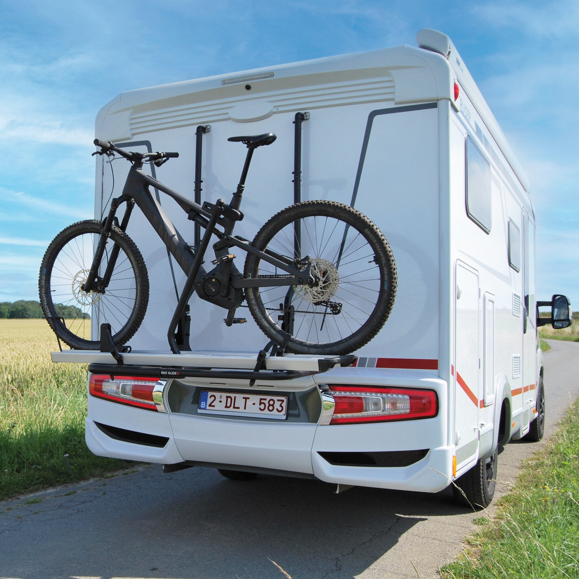 Rückansicht eines weißen Wohnmobils mit Bike Glide Fahrradträger am Heck, zwei Mountainbikes montiert, blauer Himmel und Landschaft im Hintergrund