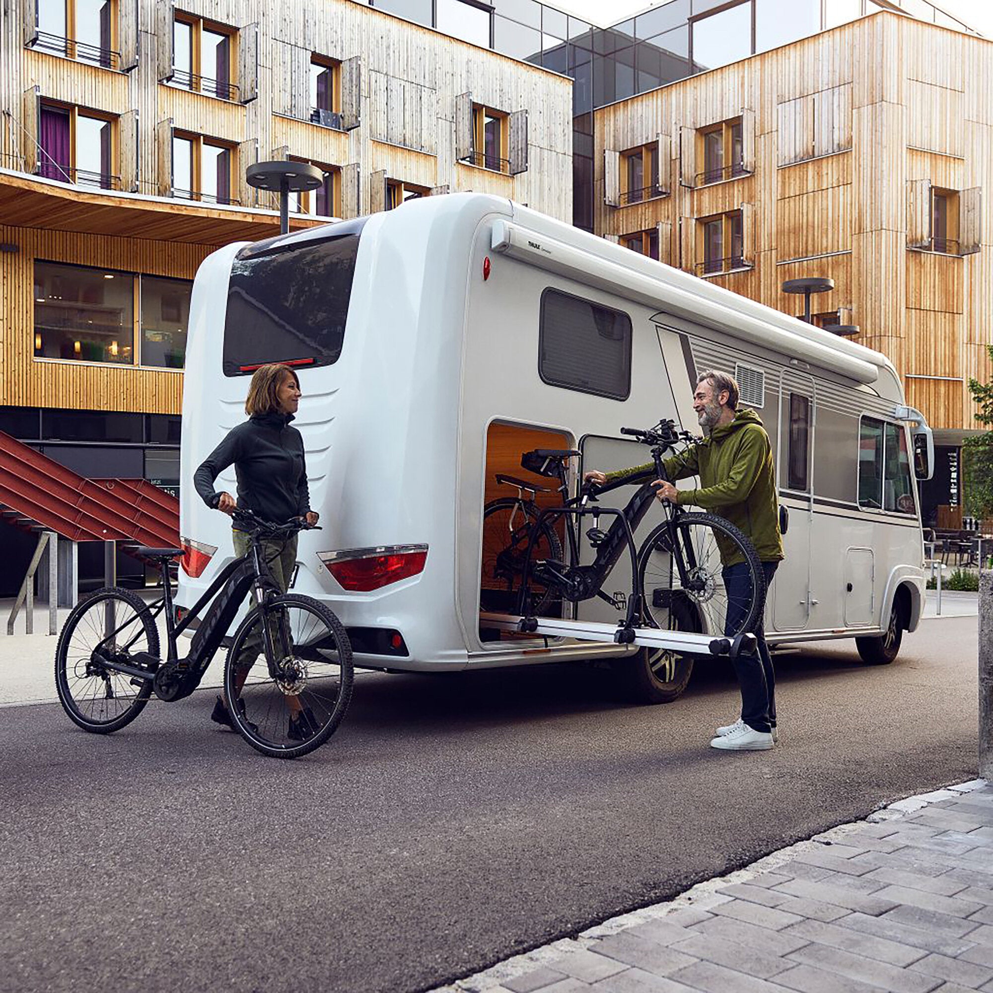 Wohnmobil mit am Heck montiertem Thule VeloSlide Short Version Fahrradheckträger, zwei Fahrräder befestigt, zwei Personen daneben