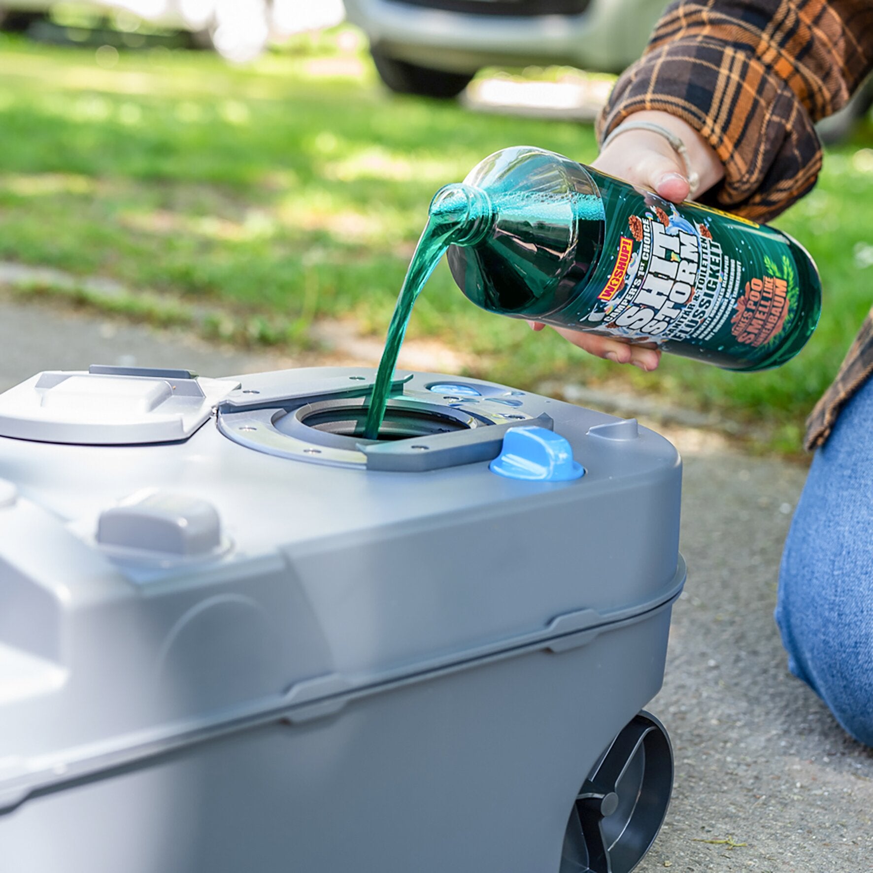 Person in kariertem Hemd gießt grünen Flüssigreiniger aus einer Flasche mit Shitstorm-Tanne-Label in eine Toplader-Waschmaschine im Freien