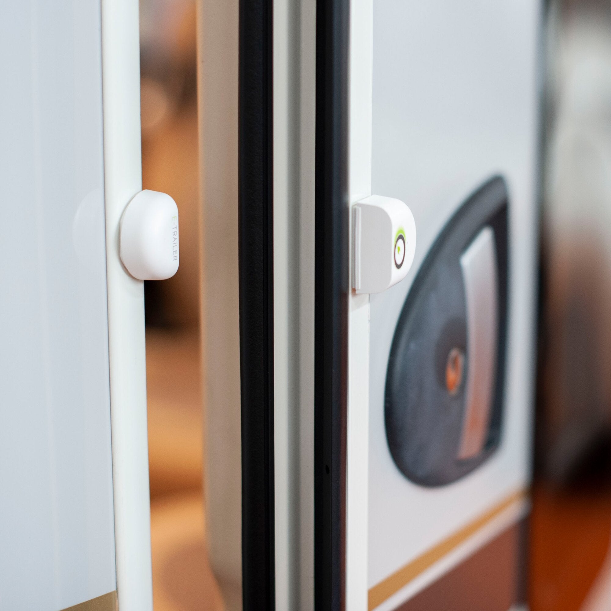 Nahaufnahme eines weißen Tür- oder Fenstersensors am Türrahmen, zwei Gehäuseabschnitte im Vordergrund, deutlich sichtbare Kanten und unscharfer Hintergrund