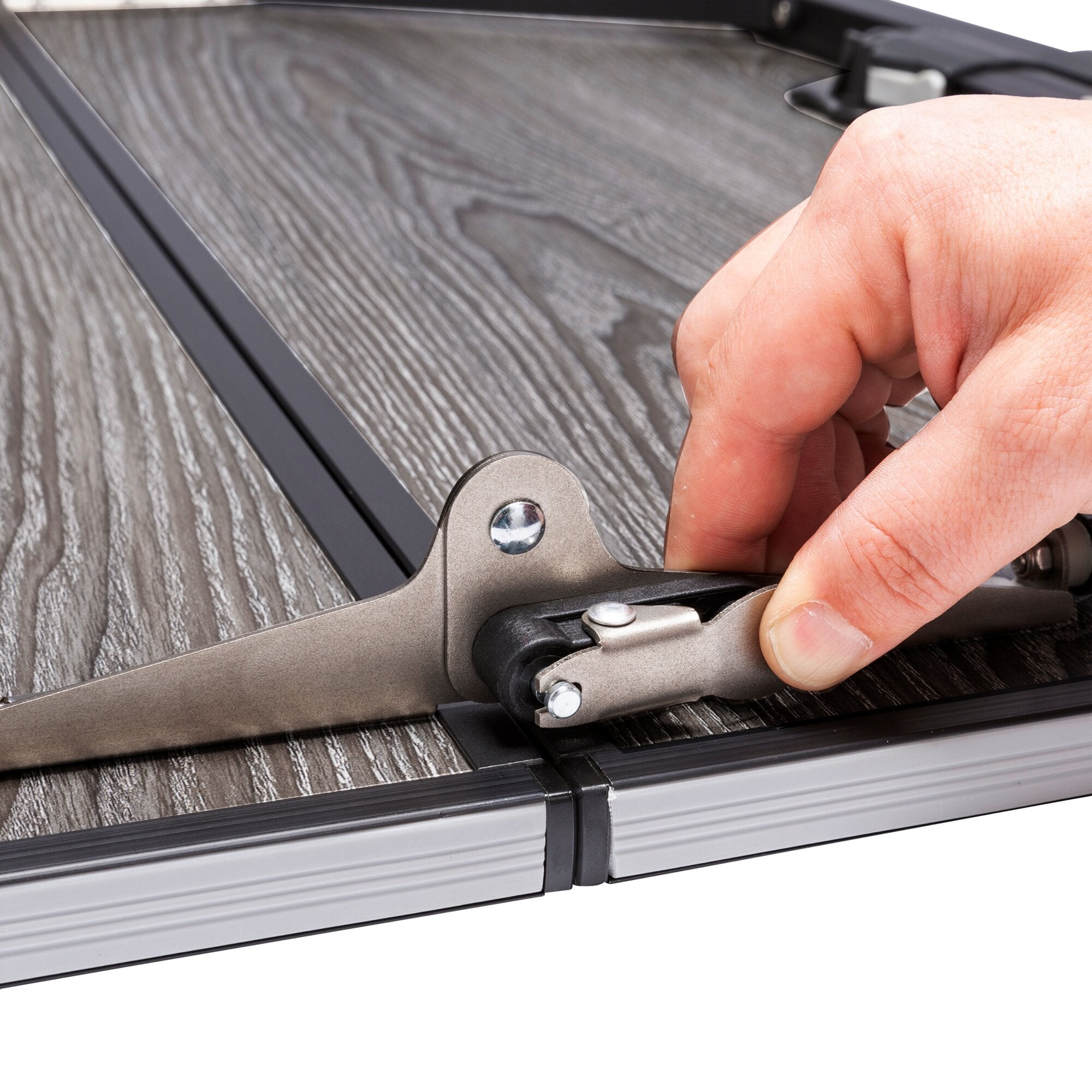 Detailaufnahme eines Campingtisch ComPack Square: graues Metallgestell, Schraubverbindung, Hand an Gelenkverbindung, Tischplatte Holzoptik