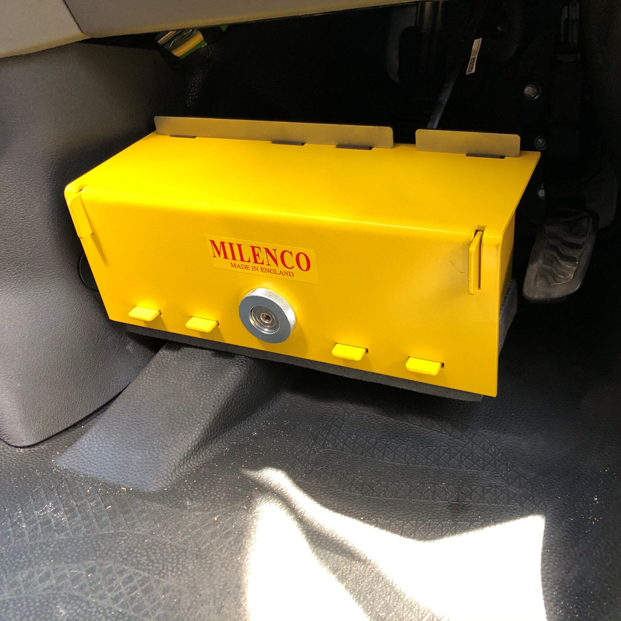 Gelbes Metallgehäuse mit Zylinderschloss an der Front, Milenco MADE IN ENGLAND-Aufkleber, im Fahrzeuginnenraum hinter dem Sitz montiert