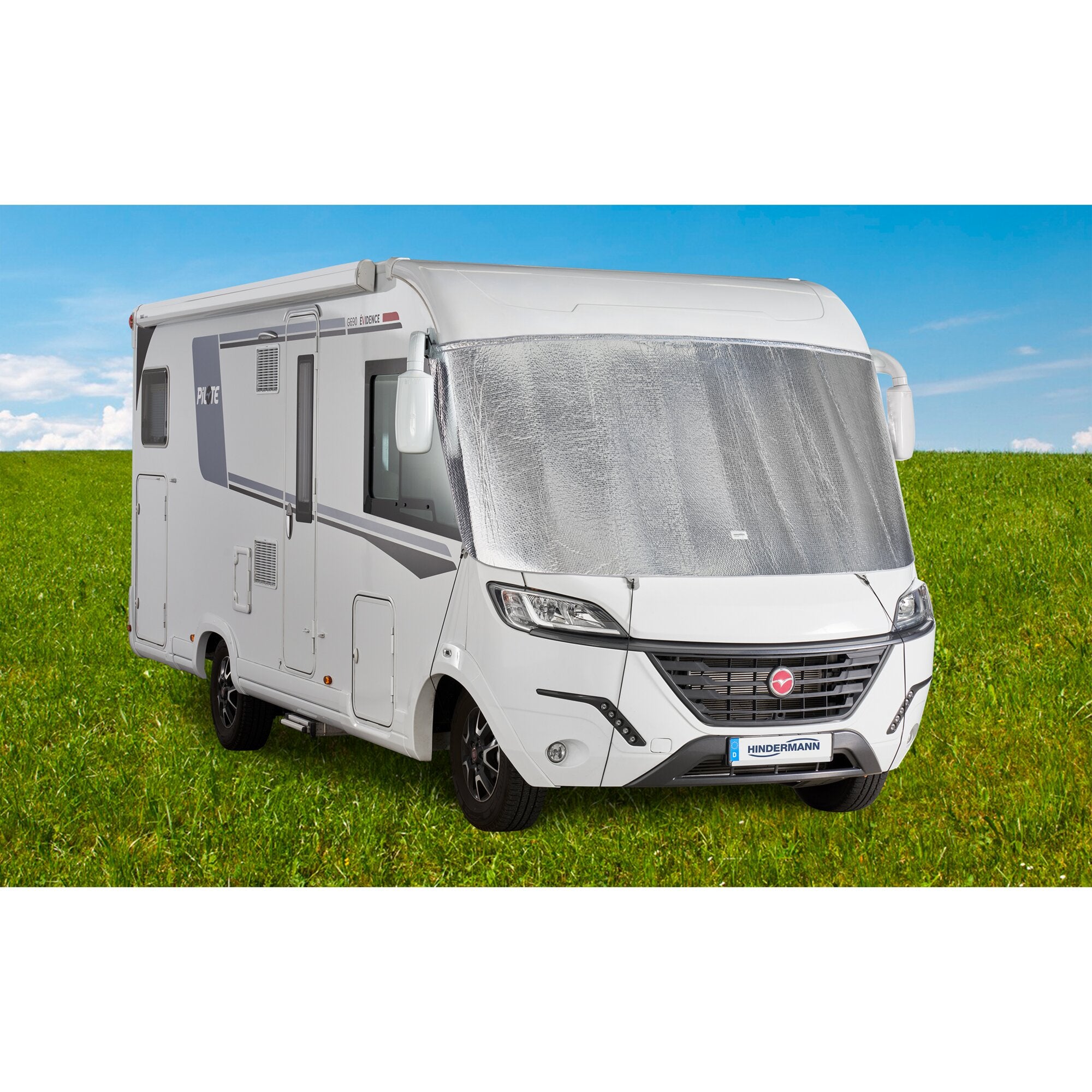 Weißes Wohnmobil mit silberner Frontscheibenisolierung, die die Windschutzscheibe bedeckt, davor grüne Wiese und blauer Himmel