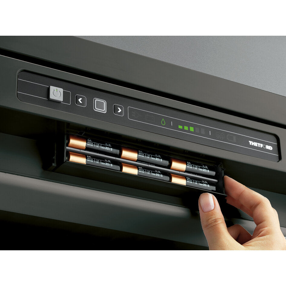 Hand platziert ein vierzelliges Batteriepack in einen Schlitz eines schwarzen Gehäuses mit Bedienfeld; grüne LEDs, Power-Taste, Pfeil- und Quadratknopf; Thetford-Logo rechts