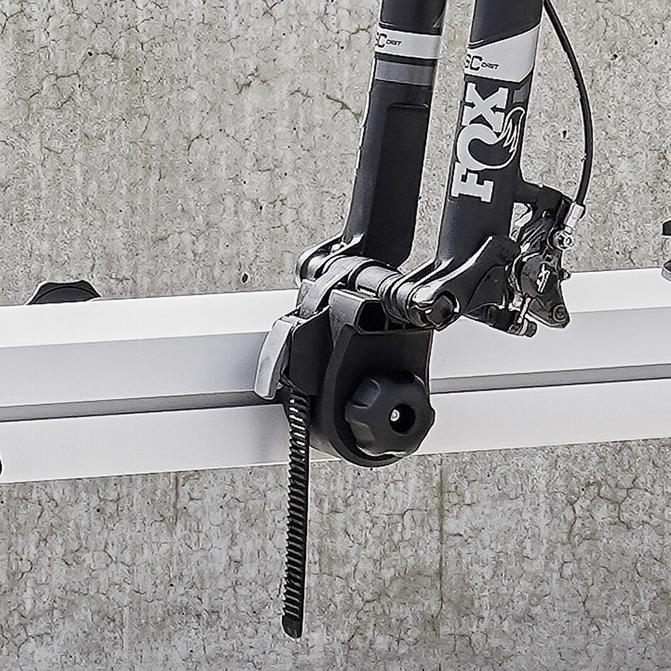 Frontgabel eines Fox-Mountainbikes mit Thru-Axle Fork Mount Adapter, montiert an einer weißen Dachträger-Querstange; sichtbare Klemmen und ein zahniges Spannband