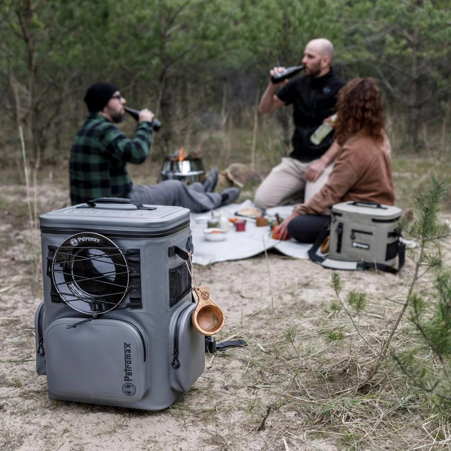 Grauer Petromax Kühlrucksack aus robustem Material mit seitlichem Lüfter und mehreren Außentaschen, steht auf grasigem Boden